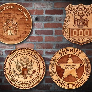 May include: Four wooden plaques with engraved designs. One reads "Minneapolis - St. Paul District Office" with a map of Minnesota. Another is a police badge with "City of Peekskill Police" and "000 N.Y." The third says "United States Pretrial Services Southern District of California." The last says "Sheriff Angelina County John Q. Public."
