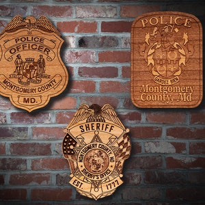 May include: Three wooden plaques with a police officer, sheriff, and police department insignia. The plaques are all engraved with the words "Montgomery County, MD".