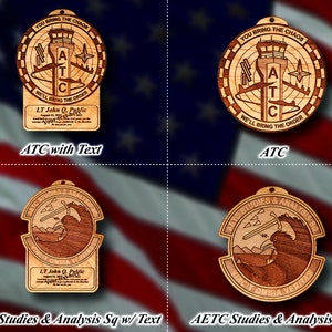 May include: Four wooden ornaments with different designs. The top left ornament features a tower with airplanes and the text "You bring the chaos, we'll bring the order". The top right ornament is the same design but without the text. The bottom left ornament features a bird with mountains and the text "AETC Studies & Analysis Sq. Omnia Veritas". The bottom right ornament is the same design but without the text.
