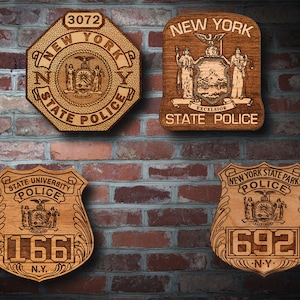 May include: Four wooden plaques with engraved New York State Police badges. The top left plaque has the number 3072 and the words "New York State Police". The top right plaque has the words "New York State Police" and the state seal of New York. The bottom left plaque has the words "State University Police" and the number 166. The bottom right plaque has the words "New York State Park Police" and the number 692.