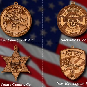May include: Four wooden ornaments featuring law enforcement badges. The top left ornament is a round badge with the text "Coles County S.W.A.T. Crisis Response Team". The top right ornament is a round badge with the text "Tidewater VCTF Violent Crimes Task Force". The bottom left ornament is a six-pointed star badge with the text "Sheriff Tulare County". The bottom right ornament is a shield-shaped badge with the text "City of New Kensington Police To Serve and Protect PA".