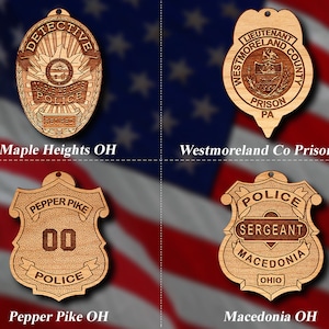 May include: Four wooden ornaments shaped like police badges. The top left ornament reads "Detective" and "Maple Heights Police Retired". The top right ornament reads "Lieutenant Westmoreland County Prison PA". The bottom left ornament reads "Pepper Pike Police 00". The bottom right ornament reads "Police Sergeant Macedonia Ohio".