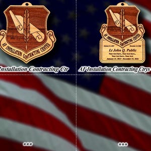May include: Wooden plaque featuring the emblem of the AF Installation Contracting Center. The emblem includes a shield, a quill, and scrolls. The text "AF Installation Contracting Ctr" is displayed. The background is the American flag.