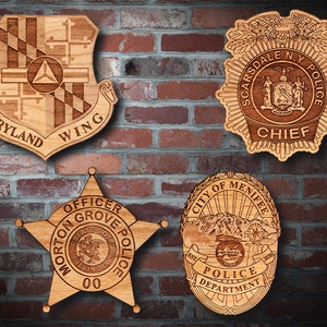 May include: Four wooden plaques with engraved designs. The top left plaque is a shield with the words "Maryland Wing" and a state flag design. The top right plaque is a police badge with the words "Scarsdale N.Y. Police Chief". The bottom left plaque is a star-shaped badge with the words "Officer Morton Grove Police" and the state of Illinois seal. The bottom right plaque is a badge with the words "City of Menifee Police Department" and a mountain scene.