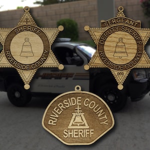 May include: Three wooden sheriff's badges with a star shape and a bell design. The badges say "Riverside County Sheriff" and "Deputy Sheriff".