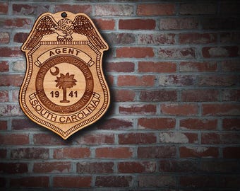 May include: Wooden Agent badge from South Carolina Probation, Parole, and Pardon Services. The badge features an eagle, the state seal, and the year 1941. The badge is hanging against a red brick wall.