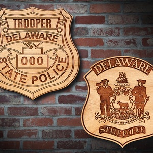 May include: Two wooden plaques with the Delaware State Police logo. The first plaque is a shield shape with the words "Trooper Delaware State Police" and the number "000". The second plaque is a shield shape with the Delaware State Seal and the words "Delaware State Police".