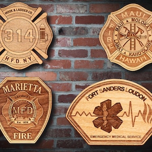 May include: Four wooden plaques with different fire department logos. The top left plaque is a red and brown fire department logo with the text "HOOK & LADDER CO 314 H.F.D. N.Y.". The top right plaque is a brown fire department logo with the text "MAUI FIRE RESCUE MAUI A MOLOKAI LANA'I A KAHO'OLAVE HAWAII". The bottom left plaque is a brown fire department logo with the text "MARIETTA GEORGIA MFD FIRE Est. 1854". The bottom right plaque is a brown fire department logo with the text "FORT SANDERS LOUDON EMERGENCY MEDICAL SERVICE".