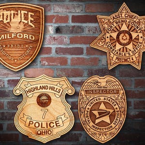 Könnte beinhalten: Vier hölzerne Polizeibadges mit unterschiedlichen Designs. Das obere linke Abzeichen ist für die Polizei von Milford, das obere rechte Abzeichen ist für das Büro des Constable von Fort Bend County, das untere linke Abzeichen ist für die Polizei von Highland Hills und das untere rechte Abzeichen ist für den United States Postal Inspection Service.
