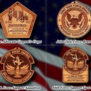 May include: Four wooden ornaments with different designs. The top left ornament is a pentagon shape with a quote about having a thousand things to do. The top right ornament is round with an eagle and the text "Joint Task Force-Bravo Progress Through Unity". The bottom left ornament is round with an eagle and the text "Serve Honor Sustain 66th Force Support Squadron". The bottom right ornament is round with an eagle and the text "Serve Honor Sustain 66th Force Support Squadron Lt John Q. Public Your text here. Your text here. Your text here. January 21, 2022 - December 21, 2024".