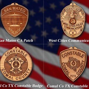 May include: Four wooden law enforcement badges with different designs. The top left badge is a brown shield with the text "SAN MATEO POLICE". The top right badge is a brown star with the text "DISPATCHER WEST CITIES POLICE COMMUNICATIONS". The bottom left badge is a brown circle with the text "CONSTABLE DEPUTY PCT 3 COMAL COUNTY TEXAS LQ PUBLIC". The bottom right badge is a brown shield with the text "CONSTABLE STATE OF COMAL COUNTY TEXAS PCT3".