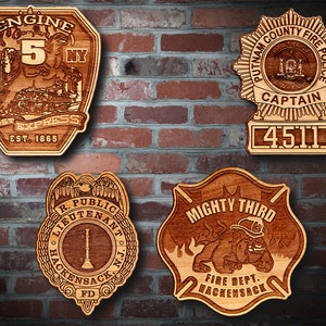 May include: Four wooden plaques with engraved designs. The top left plaque is a fire department engine badge with the text "Engine Co. FD 5 NY 145th St. Express Est. 1865". The top right plaque is a police badge with the text "Putnam County Fire Police Captain 4511". The bottom left plaque is a fire department lieutenant badge with the text "R. Public Lieutenant Hackensack N.J. FD". The bottom right plaque is a fire department badge with the text "Mighty Third Fire Dept. Hackensack".