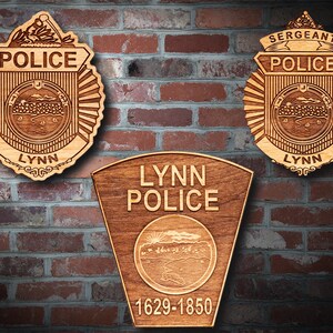 May include: Three wooden plaques with the words "Lynn Police" and "Sergeant Police" engraved on them. The plaques are decorated with a stylized image of a city skyline and the words "Lynn" and "1629-1850".