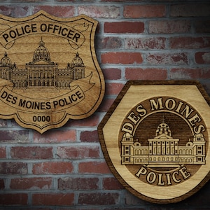 May include: Two wooden plaques with a Des Moines Police Department logo. The first plaque is shaped like a shield and says "Police Officer" and "Des Moines Police" with a building in the center. The second plaque is a hexagon with the words "Des Moines Police" around the building in the center.