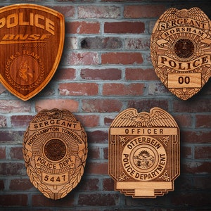 May include: Four wooden police badges with different designs and text. The badges are mounted on a brick wall. The text on the badges includes "Police", "Sergeant", "Hornsham", "Northampton Township", "Otterbein", "BNSF Railway", "K-9 Team", "Police Dept.", and "Officer".