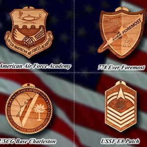 May include: Four wooden ornaments featuring military insignia. The top left ornament is a shield with the text "Inter-American Air Forces Academy". The top right ornament is a shield with the text "778 Ever Foremost". The bottom left ornament is a circle with the text "USCG Base Charleston". The bottom right ornament is a shield with the text "USSF E8 Patch".
