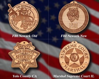 May include: Four wooden ornaments with law enforcement emblems. The top left ornament reads "FBI Newark Old" with a bear holding a gun. The top right ornament reads "FBI Newark New". The bottom left ornament reads "Yolo County CA". The bottom right ornament reads "Marshal Supreme Court IL".