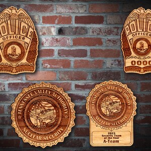 May include: Wooden plaques featuring intricate laser-cut designs. Two plaques are police badges with "POLICE OFFICER" and "ARLINGTON COUNTY" text. The other two plaques are for "TENNESSEE VALLEY AUTHORITY NUCLEAR SECURITY". One reads "2023 Security Team of the Year A-Team".