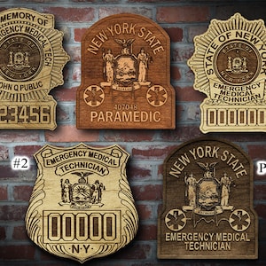 May include: Four wooden plaques with the text "New York State Emergency Medical Technician" and the state seal of New York. The plaques are in different styles and sizes, with some featuring a starburst design and others with a more traditional shield shape. The plaques are numbered 1 and 2, and one is labeled "Patch".