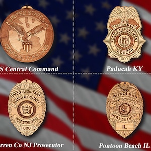 May include: Four wooden engraved badges with different designs. The top left badge is a round badge with an eagle and the text "UNITED STATES CENTRAL COMMAND". The top right badge is a star-shaped badge with the text "PATROLMAN POLICE DEPARTMENT CITY OF KENTUCKY PADUCAH 000". The bottom left badge is an oval badge with the text "FIRST ASSISTANT WARREN COUNTY STATE OF NEW JERSEY PROSECUTORS OFFICE 000". The bottom right badge is a star-shaped badge with the text "PATROLMAN PONTOON BEACH POLICE DEPT. IL".