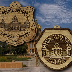 May include: Two wooden ornaments featuring the Des Moines, Iowa State Capitol building. The first ornament is shaped like a police badge and reads "Police Officer Des Moines Police 0000". The second ornament is a hexagon with the text "Des Moines Police" around the perimeter.