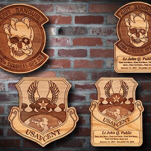 May include: Three wooden plaques with engraved designs. The top plaque features a skull with wings and the text "ERIT SANGUIS 316TH SURGICAL OPS SO". The middle plaque features a globe with wings and the text "USAFCENT". The bottom plaque features a globe with wings and the text "USAFCENT". Each plaque has a space for a name, rank, and dates of service.