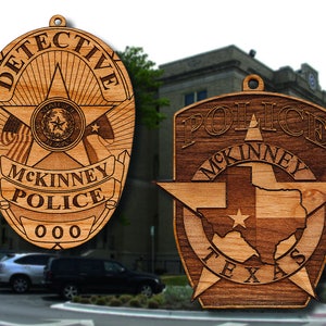 May include: Two wooden police badges with a star design. The larger badge says "Detective" and "McKinney Police 000". The smaller badge says "Police McKinney Texas".