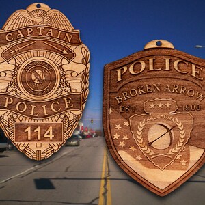 May include: Two wooden police badges, one with the text "Captain Police 114" and the other with the text "Police Broken Arrow Est. 1903 Oklahoma".