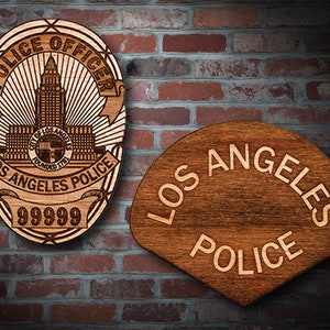 May include: Two wooden plaques with the text "POLICE OFFICER" and "LOS ANGELES POLICE" engraved on them. The first plaque features a stylized image of the Los Angeles City Hall building.