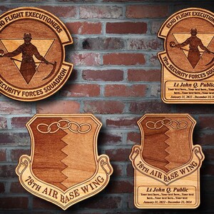 May include: Four wooden plaques with engraved designs. The top two plaques feature a circular design with the text "Echo Flight Executioners 19th Security Forces Squadron". The bottom two plaques feature a shield design with the text "78th Air Base Wing". Each plaque includes a name, rank, and dates of service.