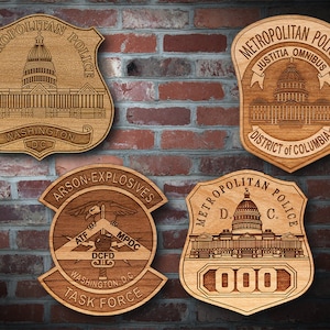 May include: Four wooden plaques with engraved images of the US Capitol building and text. The plaques are shaped like shields and feature the words "Metropolitan Police", "Justicia Omnibus", "District of Columbia", "Arson-Explosives", "ATF", "DCFD", "MPDC", "Washington, D.C.", "Task Force", and "000".