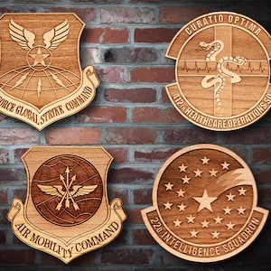 May include: Four wooden plaques featuring different Air Force unit insignia. The top left plaque reads "Air Force Global Strike Command". The top right plaque reads "Curatio Optima 412th Healthcare Operations SO". The bottom left plaque reads "Air Mobility Command". The bottom right plaque reads "22nd Intelligence Squadron".