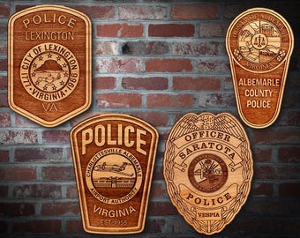 May include: Four wooden police badge plaques with intricate designs. The plaques feature text such as "Police Lexington Virginia" and "Officer Sarasota Florida Police". The badges are displayed against a brick wall.