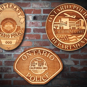 May include: Three wooden plaques with a police department theme. The top plaque is round and reads "Ontario Police Department California 1891". The middle plaque is oval and reads "Lieutenant Ontario Police 000". The bottom plaque is a shield shape and reads "Ontario Police California 1891".
