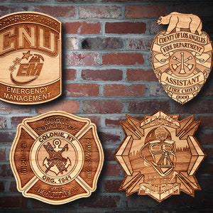May include: Four wooden plaques with laser-engraved designs. The top left plaque features the letters "CNU" and "EM" with the words "Emergency Management" below. The top right plaque features a bear, the words "County of Los Angeles Fire Department", and "Assistant Fire Chief". The bottom left plaque features a fire department logo with the words "Bogt Community Colonie, NY Fire Department Org. 1941". The bottom right plaque features a Star Wars themed design with the words "Force of the Fourth" and a depiction of Darth Vader.