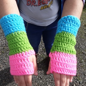 May include: A pair of colourful, handmade crochet fingerless gloves. The gloves are striped with bands of blue, green, and pink. The crochet stitch creates a textured pattern. These gloves are a vibrant accessory.
