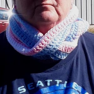 May include: A person wearing a blue shirt with the word "Seattle" on it. They are wearing a crocheted neck warmer with pink, blue, and white stripes.