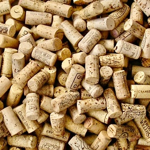 May include: A close-up image of a pile of used wine corks. The corks are made of natural cork and have a variety of colors and textures. Some of the corks have writing on them, including the names of wineries and the regions where the wine was produced.