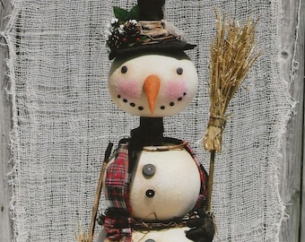 May include: A three-tiered snowman with a black top hat, a red and black plaid scarf, and a brown twig broom. The snowman is made of white fabric and has black button eyes and a carrot nose.