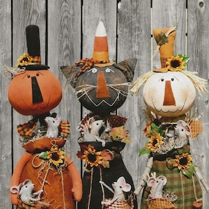 May include: Three handmade Halloween decorations, a pumpkin, a black cat, and a scarecrow, each with a hat and holding a small mouse in their arms. The decorations are made of fabric and have a rustic, vintage look.