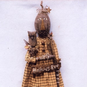 May include: A handcrafted Halloween doll with a pumpkin-shaped head, wearing a plaid dress and holding a sign that reads "Hallows Eve." The doll has an owl companion and is adorned with rustic details, including a star and twig accents.