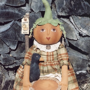 May include: A handmade pumpkin doll wearing a plaid dress and holding a pie. The doll has a black bird perched on its shoulder and is sitting on a wooden chair. The doll has a sign that says "Pretty as Pie".