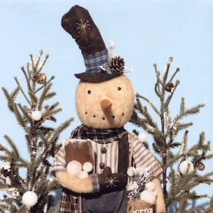 Puede incluir: Un muñeco de nieve hecho a mano que lleva una camisa a cuadros, un mono y un sombrero marrón con una banda a cuadros. El muñeco de nieve sostiene una pala y un saco de arpillera que dice "Snow Collector". El muñeco de nieve está de pie frente a dos pequeños pinos.