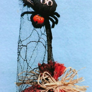 Puede incluir: Una decoraci&oacute;n de calabaza de Halloween hecha a mano con una ara&ntilde;a negra en la parte superior, una tela estampada en blanco y negro y un lazo de paja marr&oacute;n.