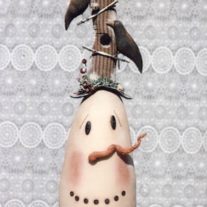 May include: A whimsical snowman figurine with a birdhouse hat, two birds perched on the roof, and a brown felt mustache. The snowman is decorated with red berries and a green garland.