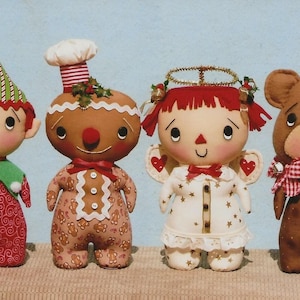 May include: Four handmade Christmas ornaments: a gingerbread person, an elf, an angel, and a brown bear. The gingerbread person is wearing a red bow and has a white icing design. The elf is wearing a green hat with red and white stripes, a green shirt, and red pants. The angel is wearing a white dress with gold stars and a gold halo. The bear is wearing a red and white plaid scarf and a red Santa hat. The bear is holding a red heart with the word "Christmas" on it.