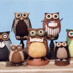 May include: A collection of six handmade owl figurines. The owls are made of fabric and have different patterns and colors. They are all sitting on small stands. The owls have large eyes and are very cute.
