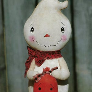 以下が含まれることがあります： クリーム色の布製ゴーストの置物。手描きされた顔にはバラ色の頬、小さなオレンジ色の鼻、大きな笑顔が描かれています。ゴーストは黒い文字が入った赤いスカーフを巻き、黒い顔とチェック柄のリボンが付いた赤い布製のカボチャを持っています。