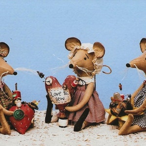 May include: Three handmade fabric mouse dolls with embroidered details. The mouse in the center is holding a red heart with the text "Love to sew". The mouse on the left is holding a red heart with buttons and the mouse on the right is holding a spool of thread and other sewing supplies.