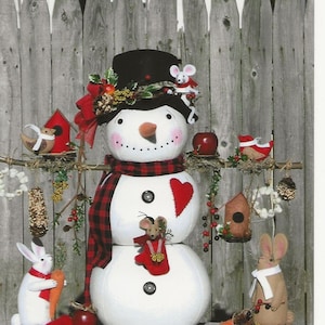 May include: A white snowman with a red and black plaid scarf, a red heart, and a black top hat. The snowman is decorated with a wreath of greenery, red berries, and a small mouse. There are also two small white rabbits and a brown rabbit with a white scarf.